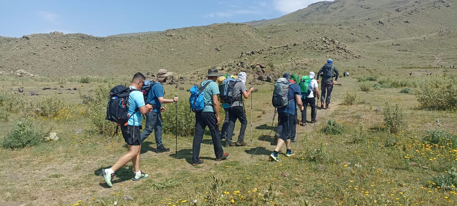 Kolona s velikim rančevima kreće travnatom stazom prema kamenitim padinama planine.